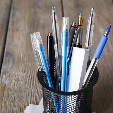 Pens in metal holder on wooden desk