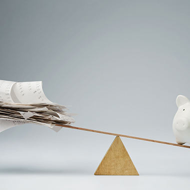 Piggy Bank Balancing on Seesaw Over Bills