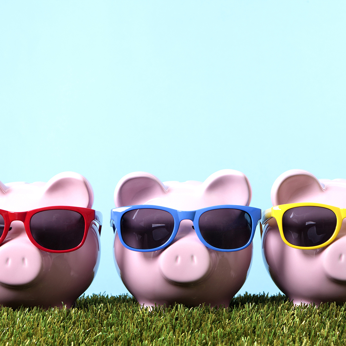 Three pink piggy banks with sunglasses on grass with blue sky