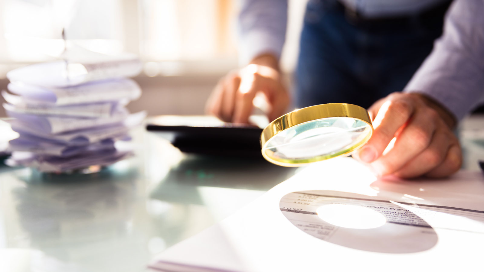 Business person hand analyzing bill through magnifying glass