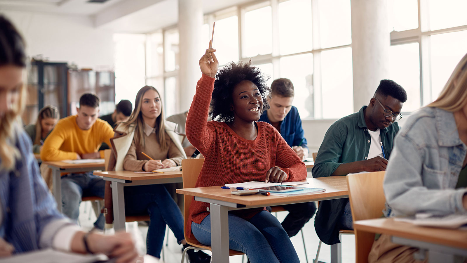 Happy student raising arm to answer question while attending class with her university collegues