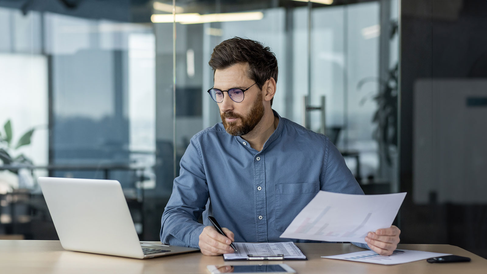 Serious financier working on paperwork and analyzing data in modern office