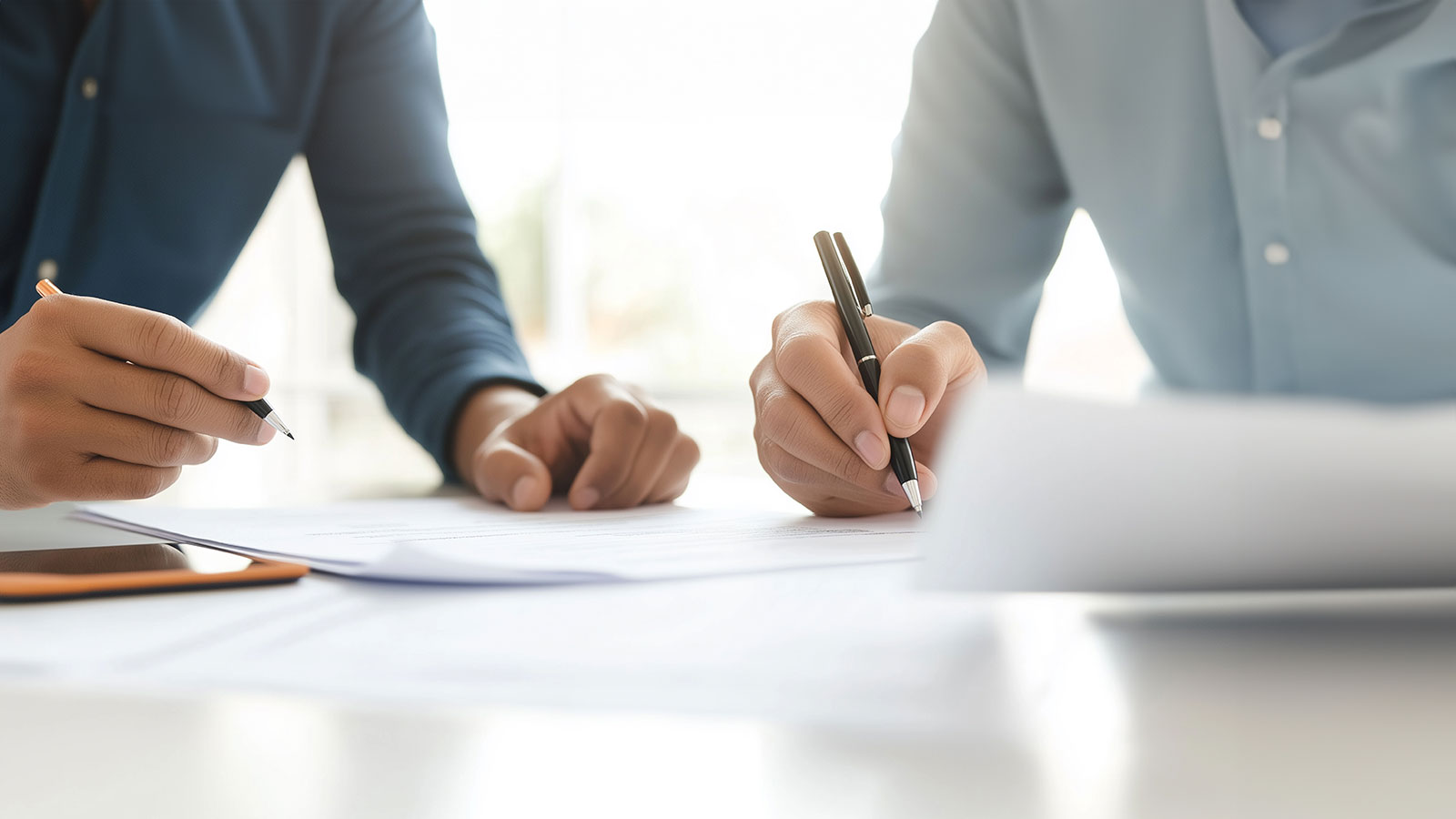 Two people writing and reviewing documents together at a desk.