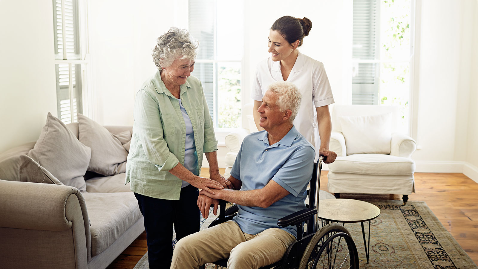 Smile, old man in wheelchair with wife and nurse at nursing home for disability help and rehabilitation