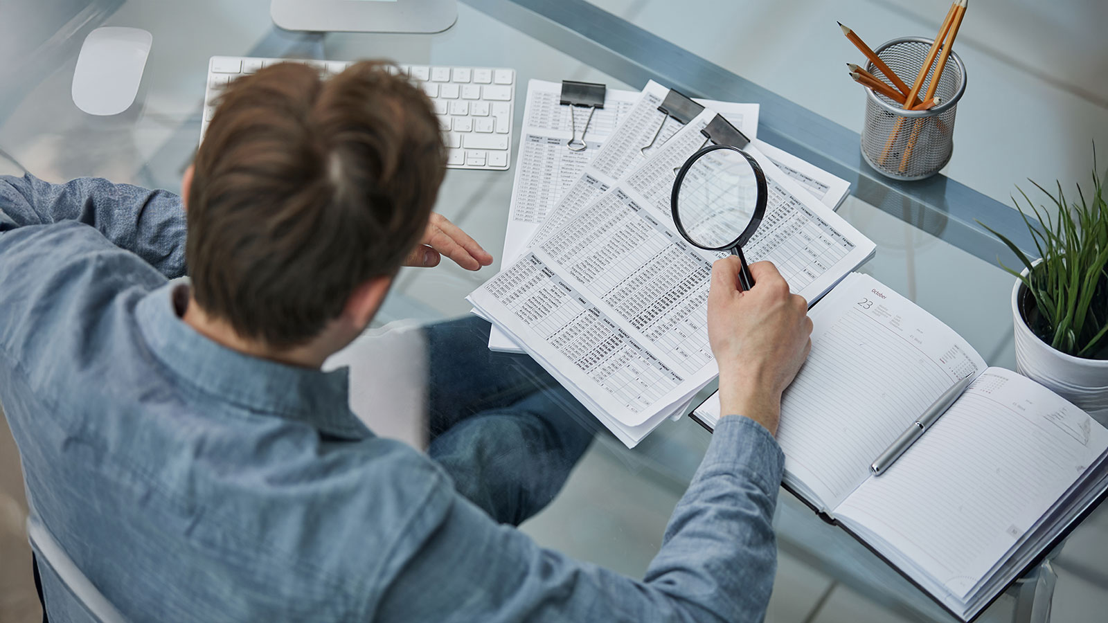 Businessman looking through a magnifying glass to documents note in the office.