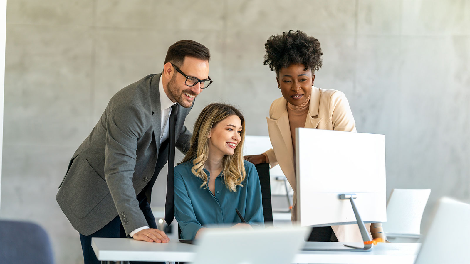 Group of business people in formal wear gathered around computer in office