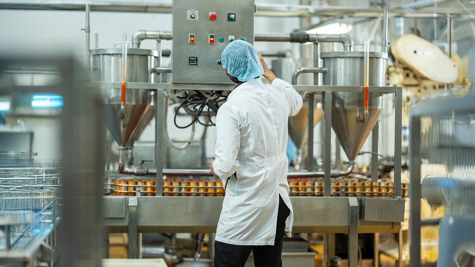 Worker inspecting automated equipment and canned products in a clean production facility