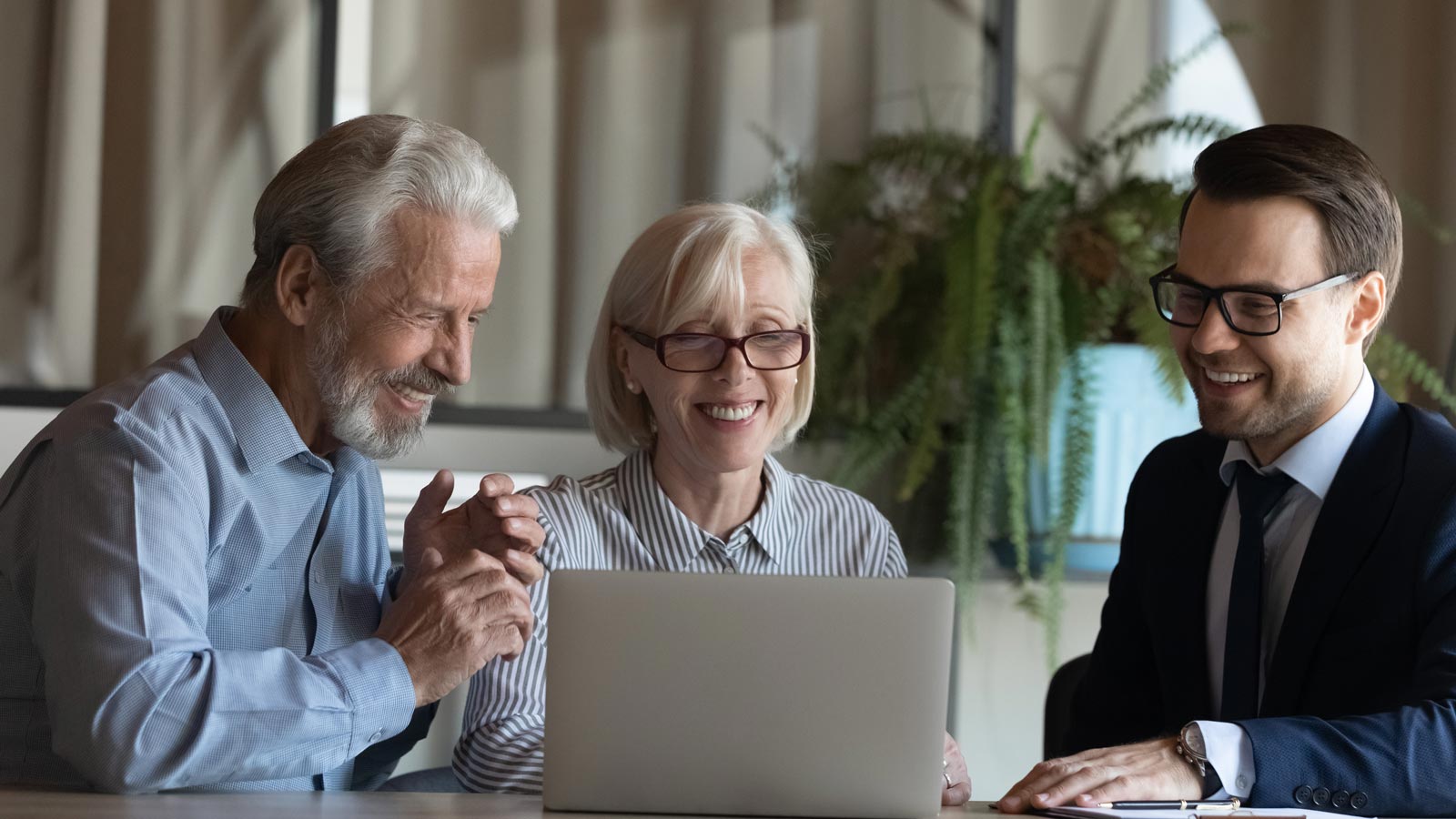 Smiling male realtor or broker consult middle-aged couple buyers show project on laptop