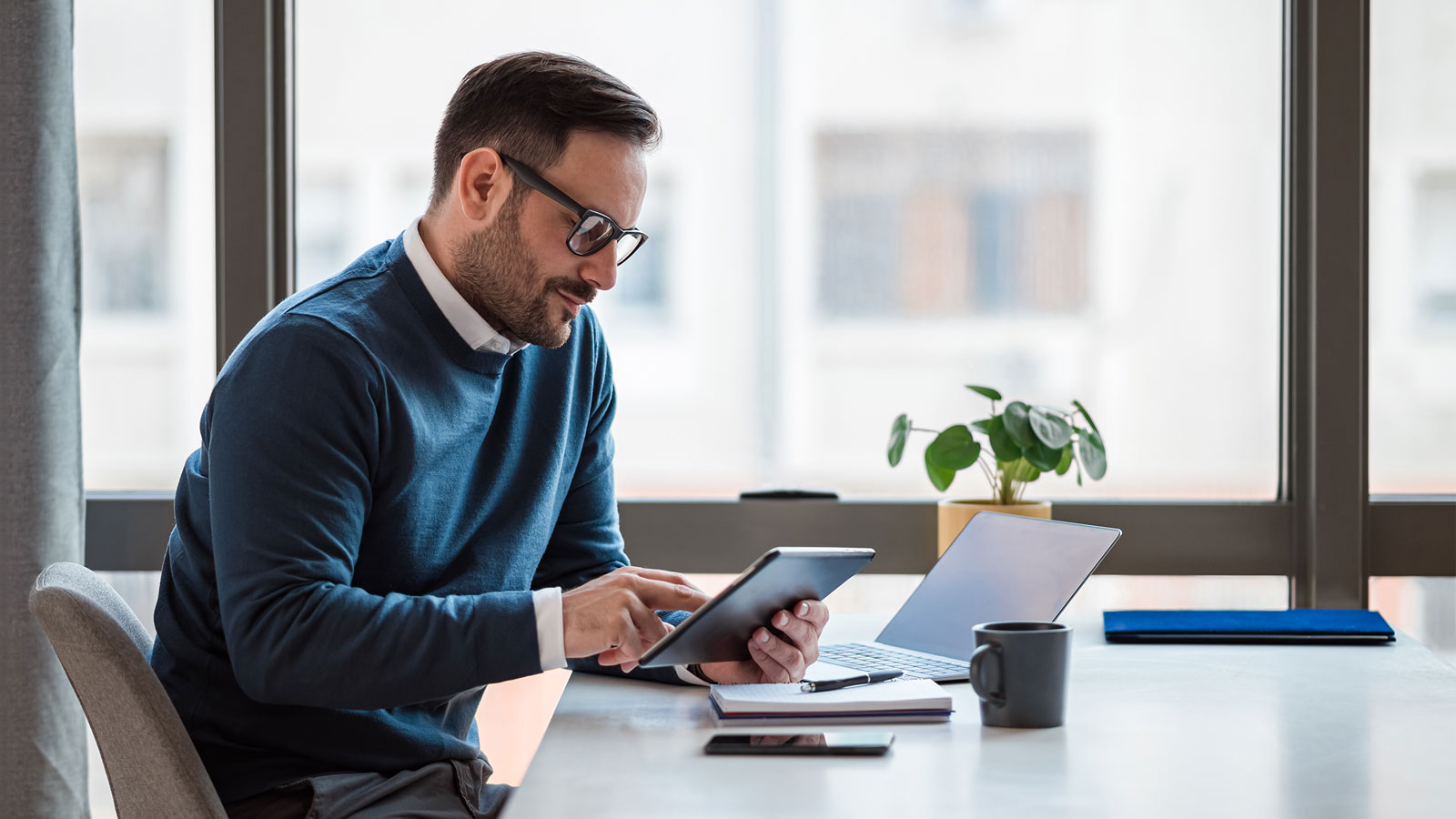 Businessman using digital tablet while working on laptop at office desk