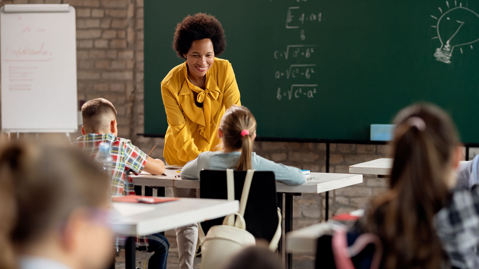 Happy elementary school teacher taking to her students in the classroom